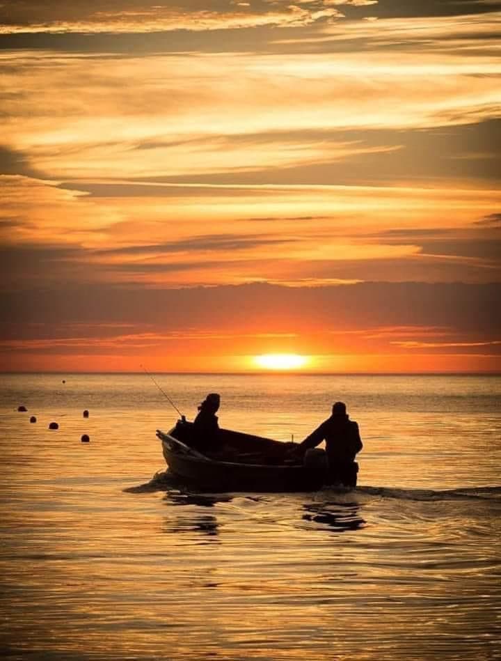 Two people in a small boat against an orange sunset